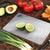 A Small Cutting Board with a halved lime, avocados, tomatoes, and green onions.