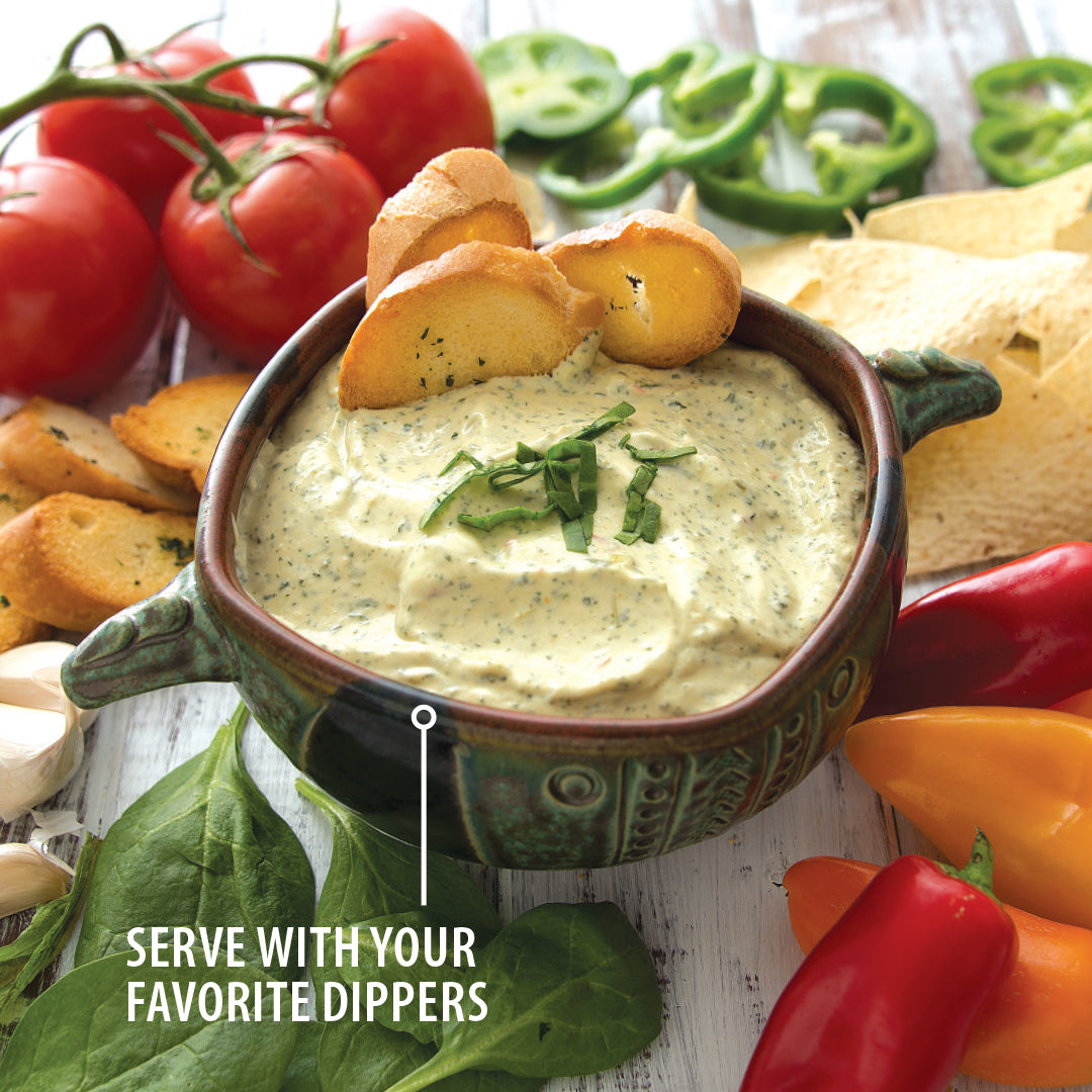 A bowl of Spinach Artichoke Dip with baguette slices next to tomatoes, peppers, chips, and spinach.