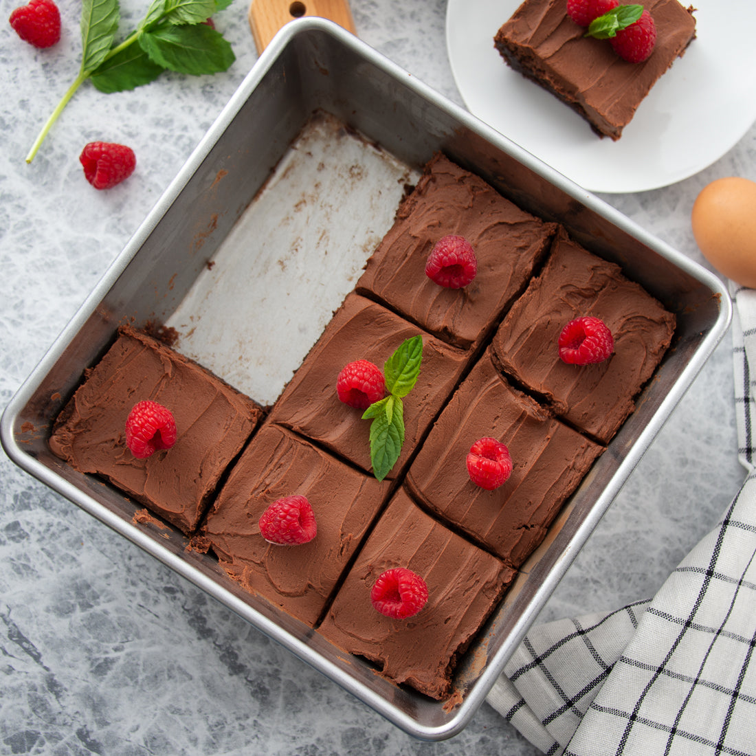 A Square Pan filled with raspberry-topped chocolate brownies on a marble counter. 