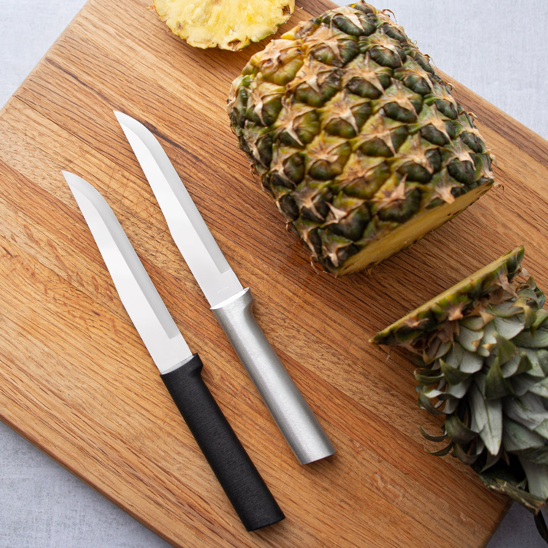 Silver and black handle Rada Stubby Butcher laying on a cutting board with a sliced pineapple.