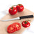 Silver handled tomato slicer on a tan cutting board next to sliced and whole tomatoes.