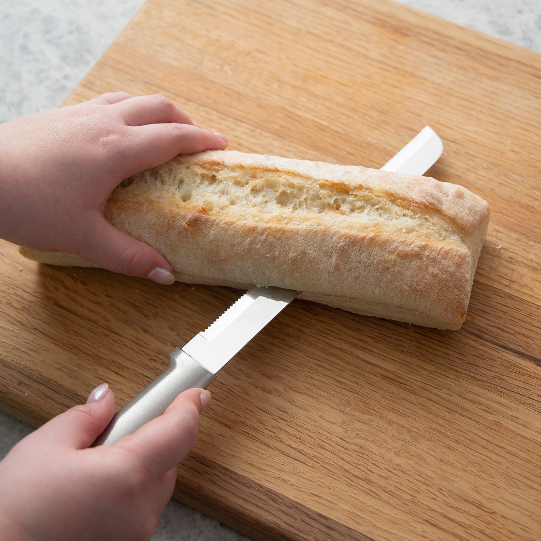 The famous Rada Cutlery Bread Knife on a cutting board, slicing bread in half.