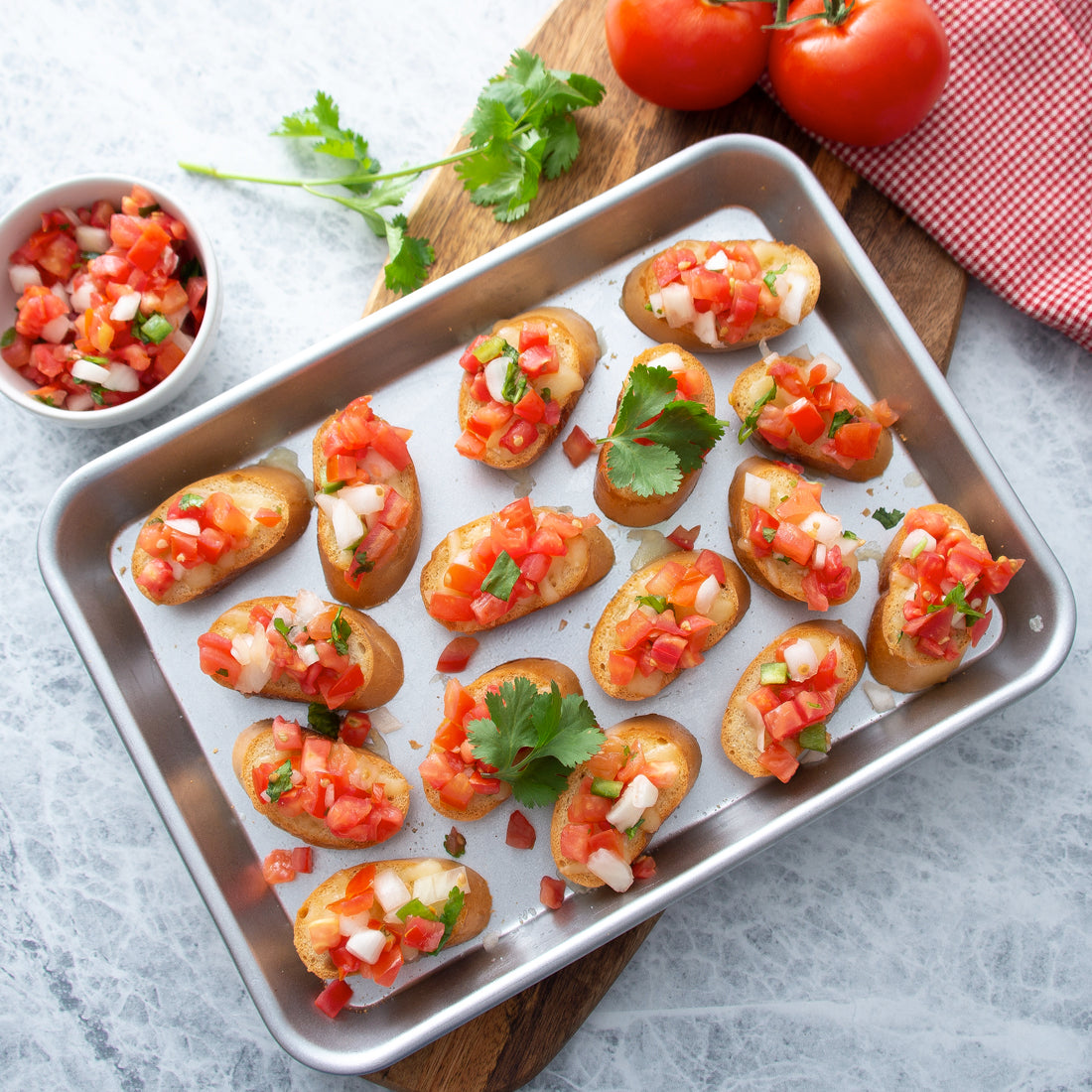A Quarter Sheet Pan from Rada Cutlery showing bruschetta with tomatoes and herbs on a wood cutting board with basil, tomatoes, and a bowl of chopped tomatoes in the background.