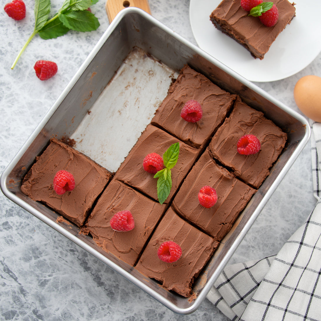 Rada Cutlery Square Pan showing chocolate cake with raspberries and mint leaves in the pan on a gray surface.