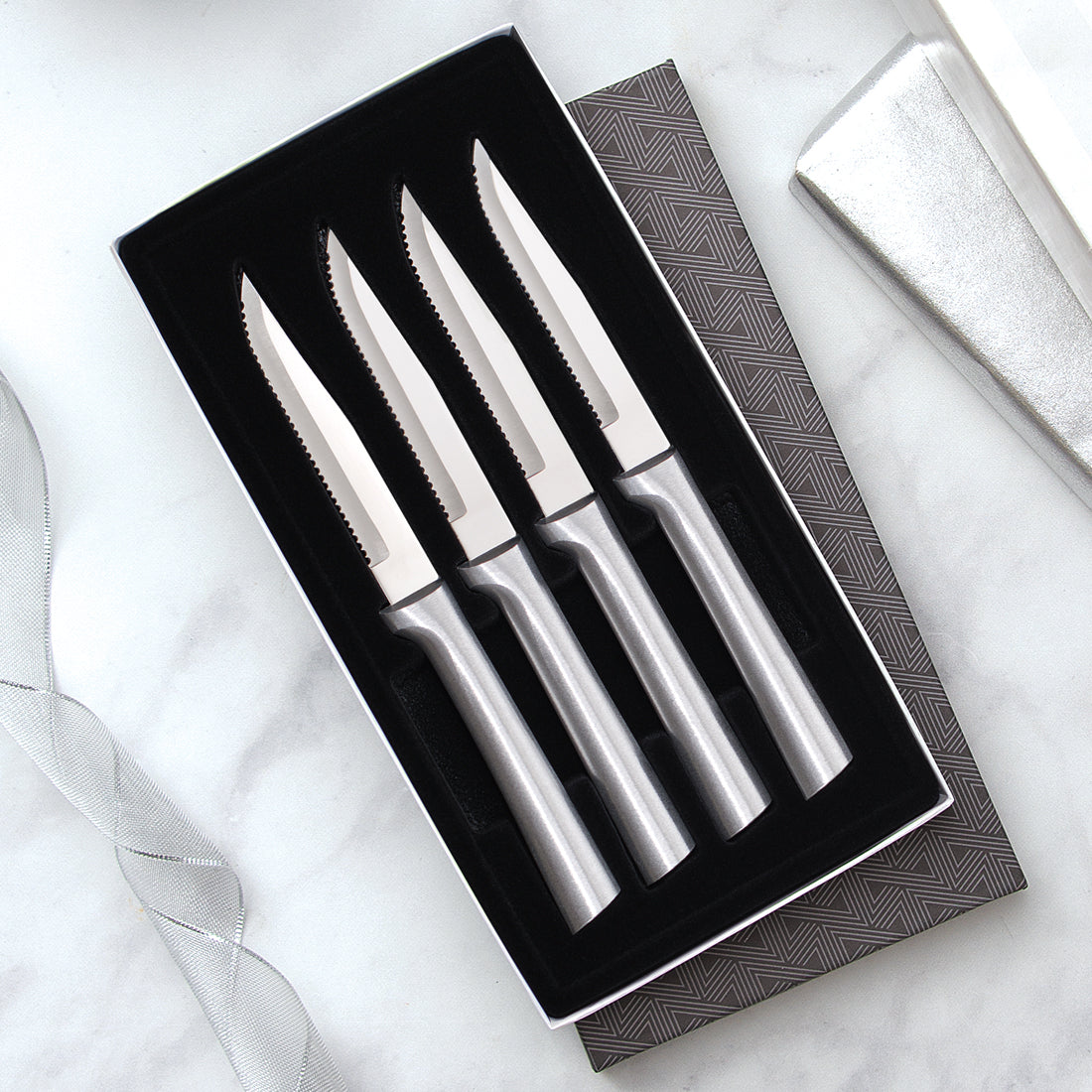 Four Serrated Steak Knives Gift Set on a marble countertop with silver ribbons