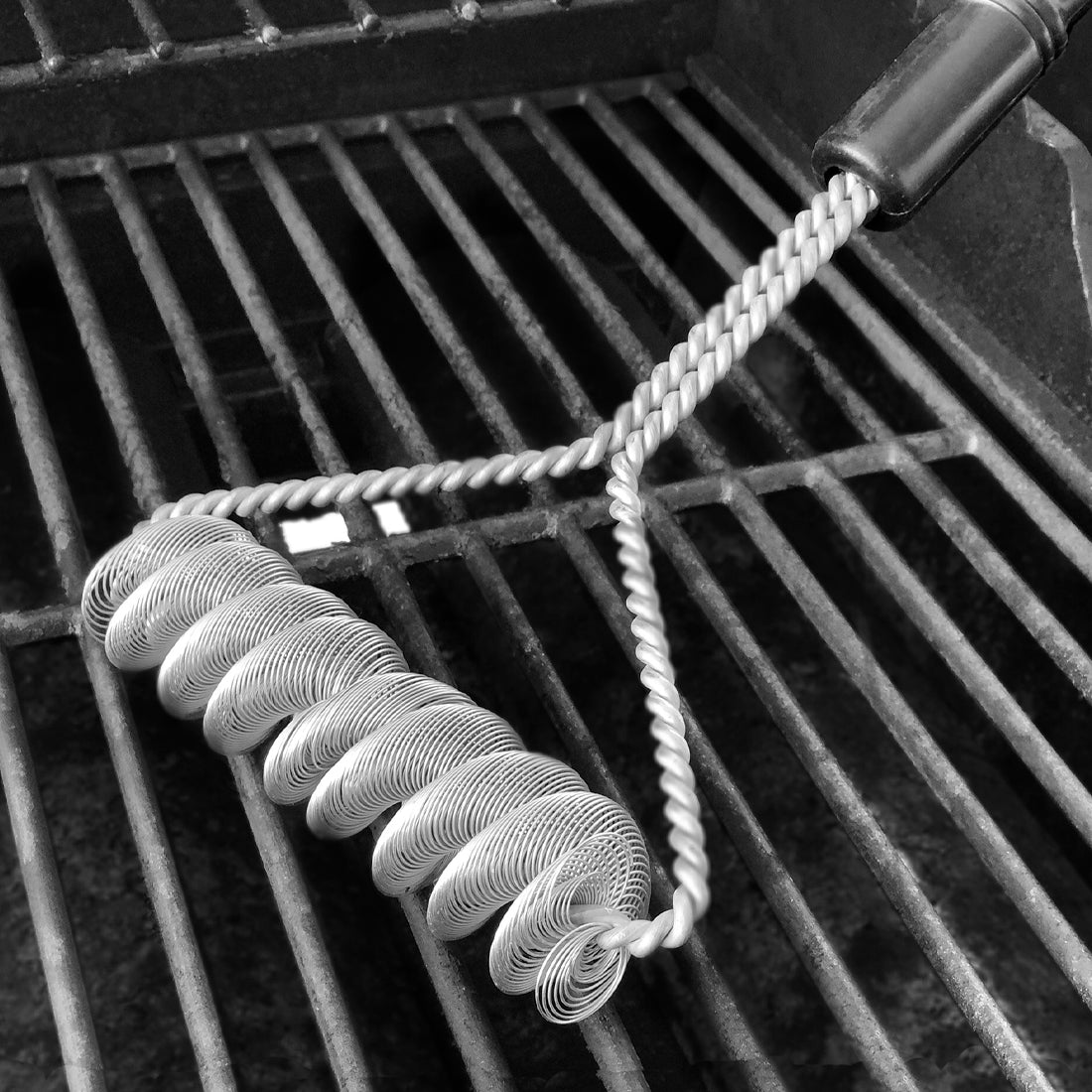 Rada Cutlery Grill Brush laying on top of grate on grill cleaning it.