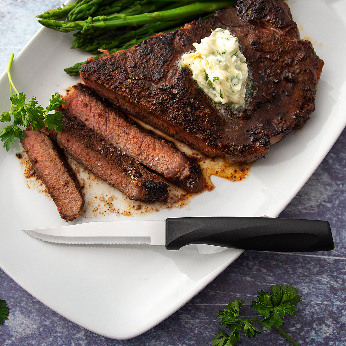 An Anthem Wave Serrated Steak Knife on a white plate with sliced meat
