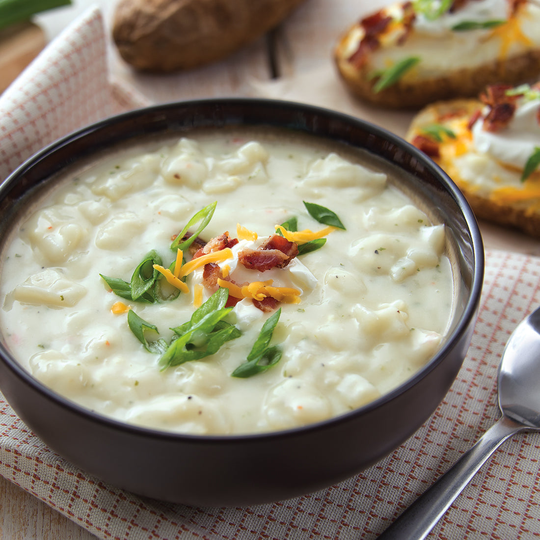 A bowl of Baked Potato Soup on a red and white tablecloth