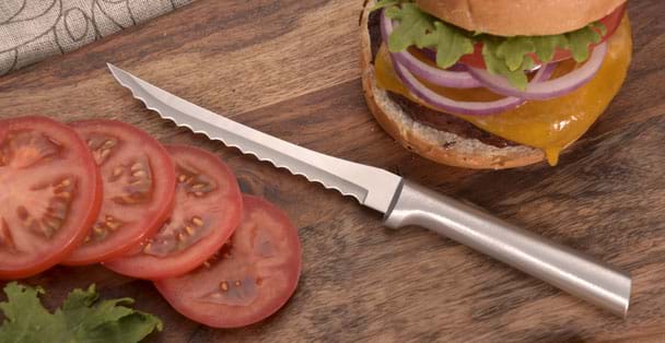 The silver handled tomato slicer by a hamburger an