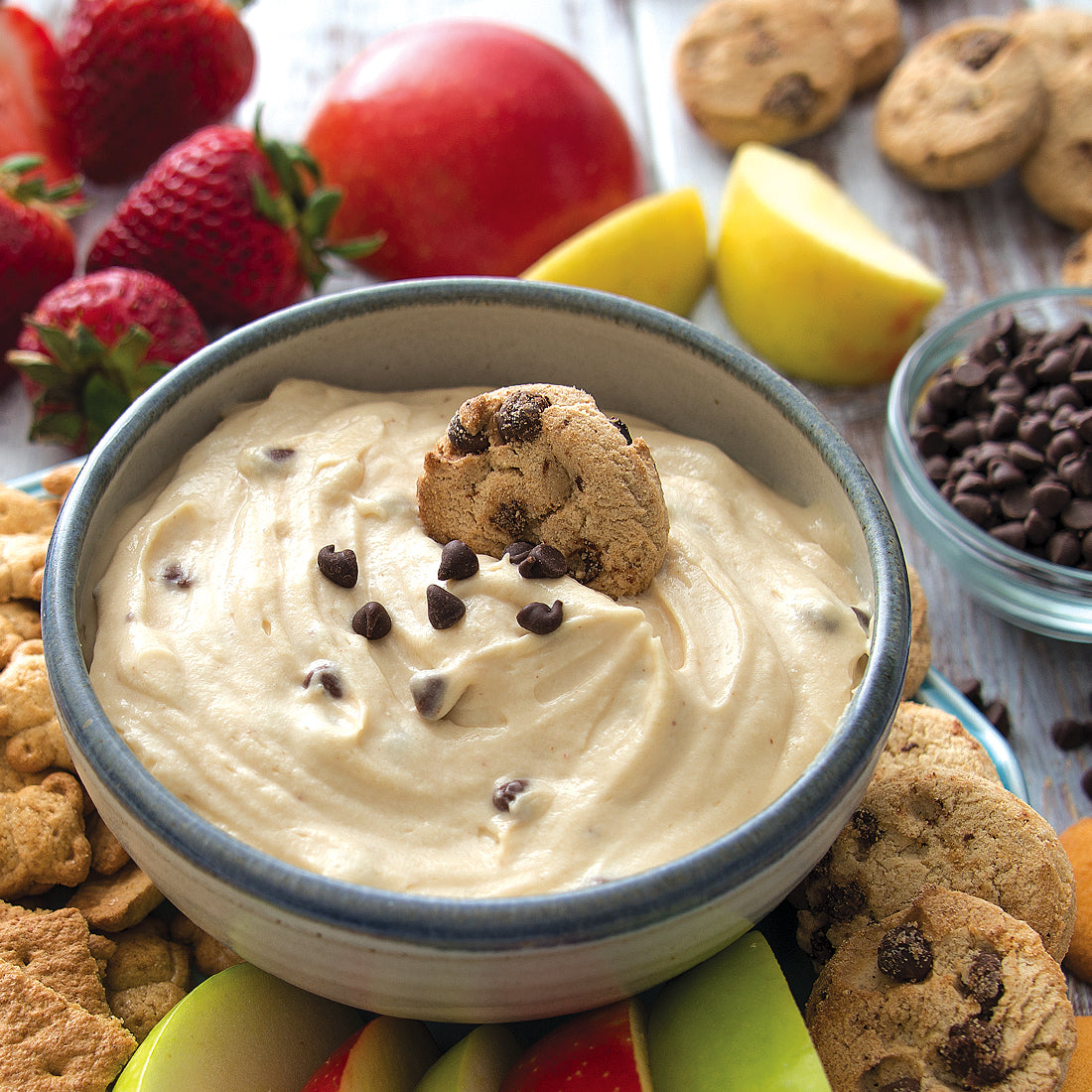 A bowl of Cookie Dough Sweet Dip surrounded by cookies and assorted fruits.