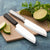 Two Cook's Utility knives on a tan cutting board with sliced limes.