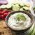 A bowl of Cucumber Onion Dill Dip next to crackers, cucumbers, and cherry tomatoes.