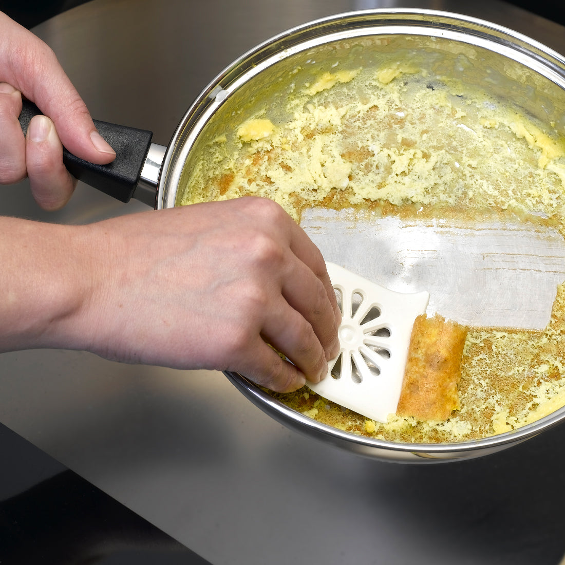 A Daisy PanMate Scraper being used to scrape egg from the bottom of a pan
