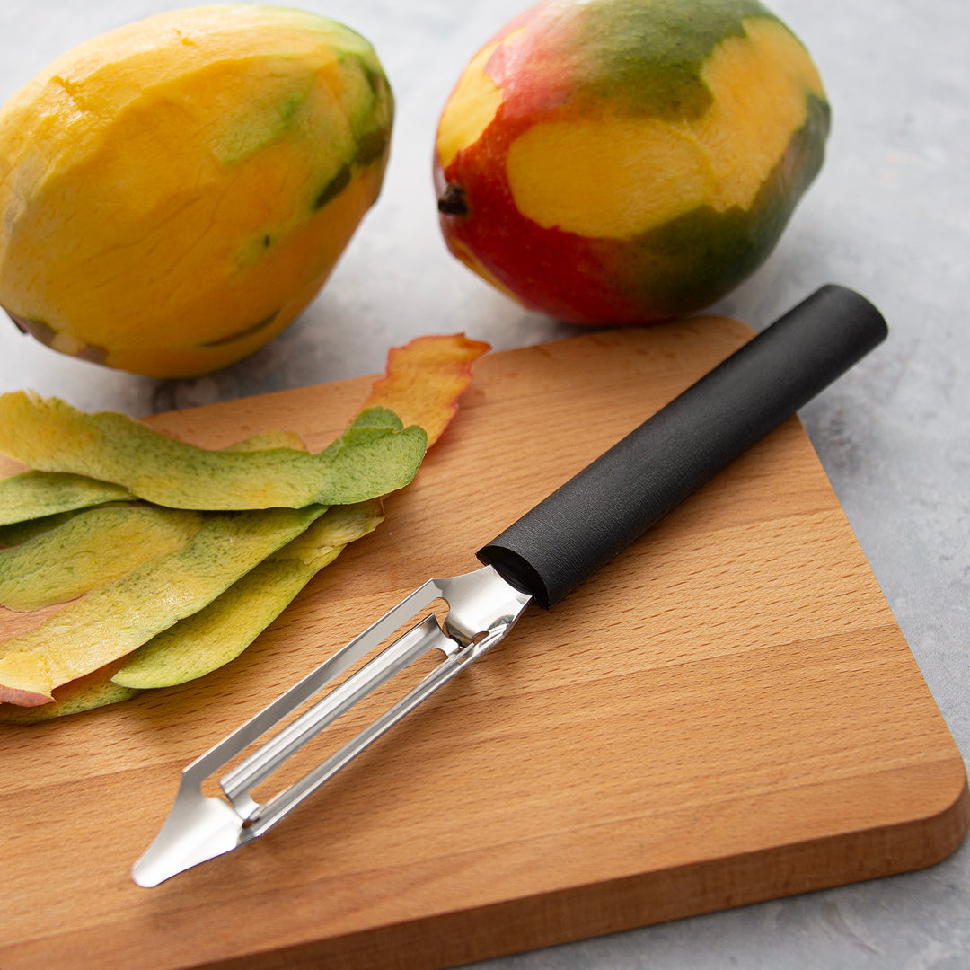 Peeled mangos next to a cutting board with a silver Deluxe Vegetable Peeler.