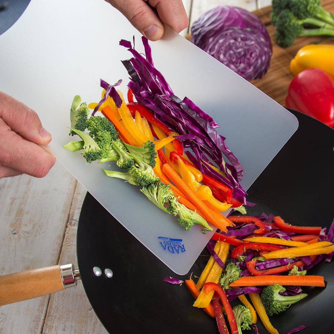 A Flexible Cutting Board being used to funnel chopped vegetables into a wok