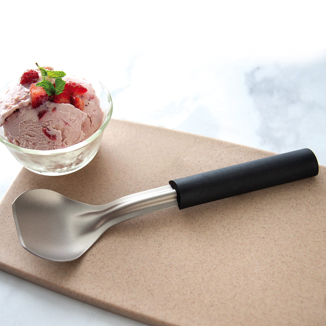 An Ice Cream Scoop next to a bowl of strawberry ice cream