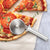 A silver handle Pizza Cutter next to a sliced pizza with tomatoes and pepperoni.