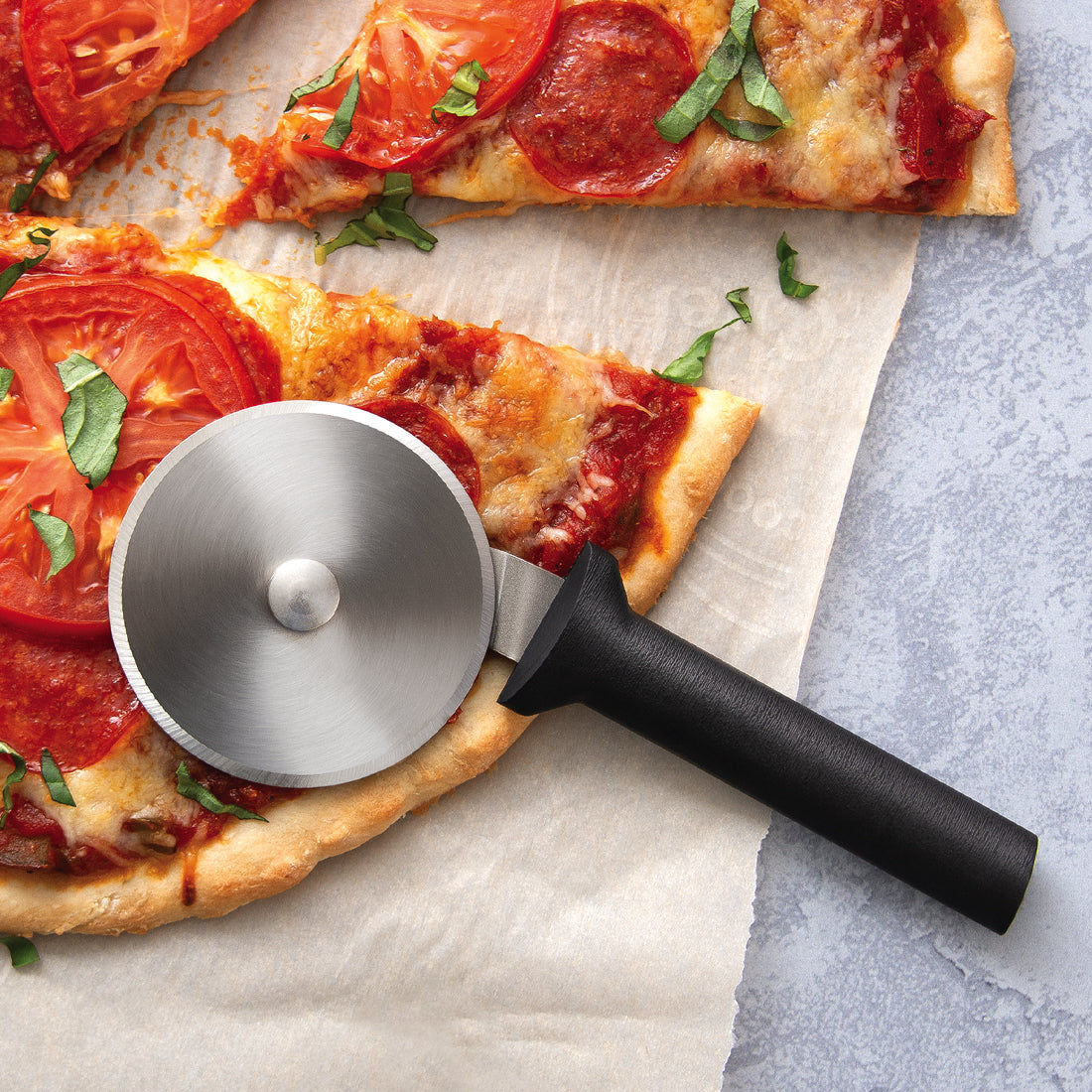 A silver handle Pizza Cutter next to a sliced pizza with tomatoes and pepperoni.