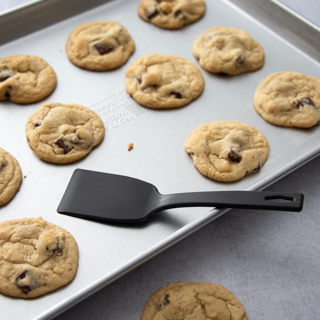 Rada's Potluck Spatula laying on a sheet pan with baked chocolate chip cookies.