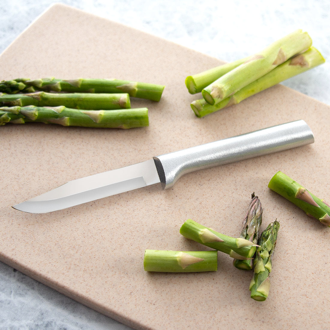 Silver handled Regular Paring knife next to sliced asparagus on a tan cutting board