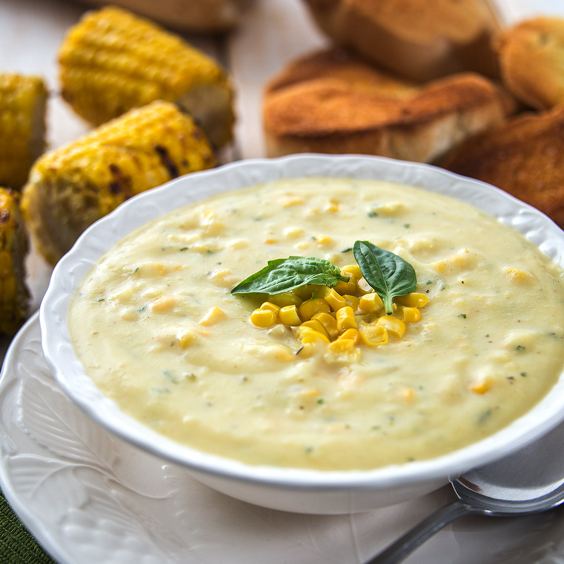 A bowl of Roasted Corn Chowder Soup with corn and bread in the background