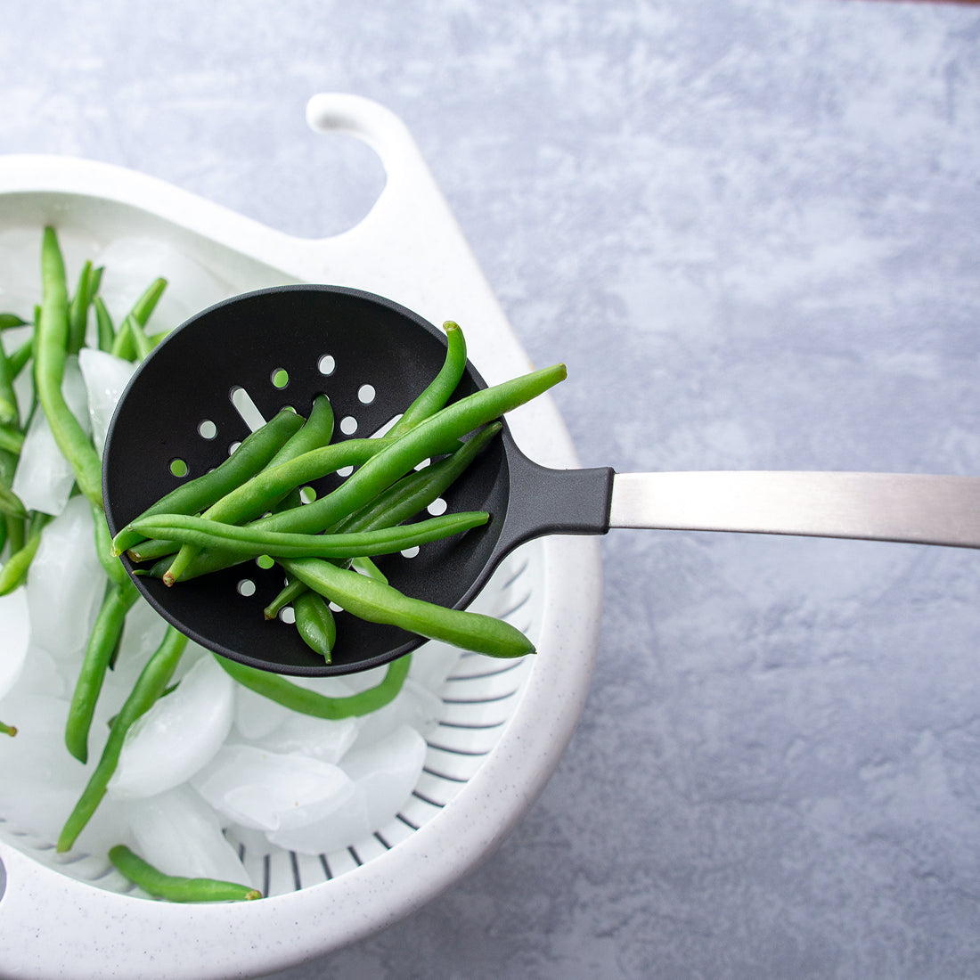Rada Cutlery non-scratch Skimmer over a colander, straining green beans.