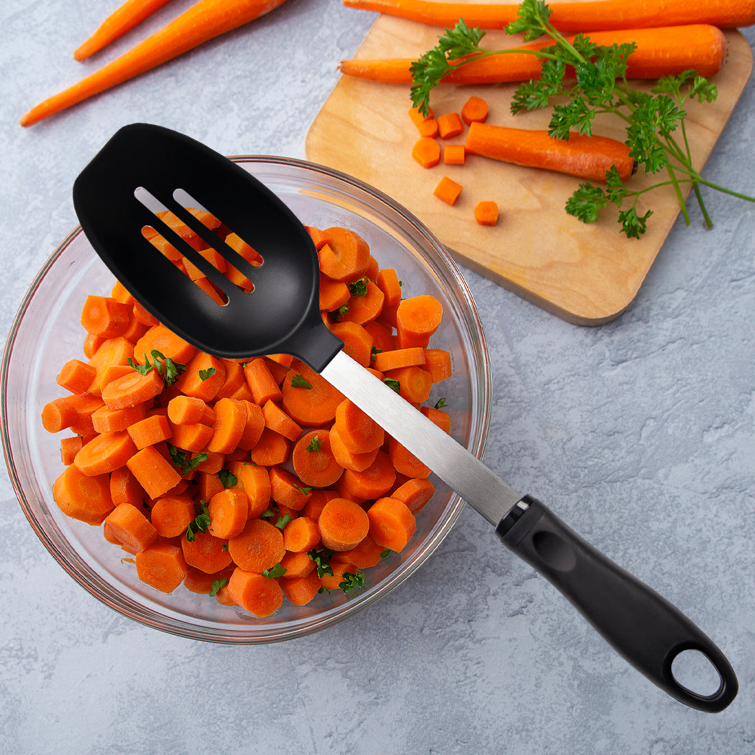 Rada Cutlery Slotted Spoon with leafy greens, peeled carrots, and cut carrots in a bowl.