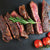 Sliced medium rare steak with a sprig of rosemary and cherry tomatoes.