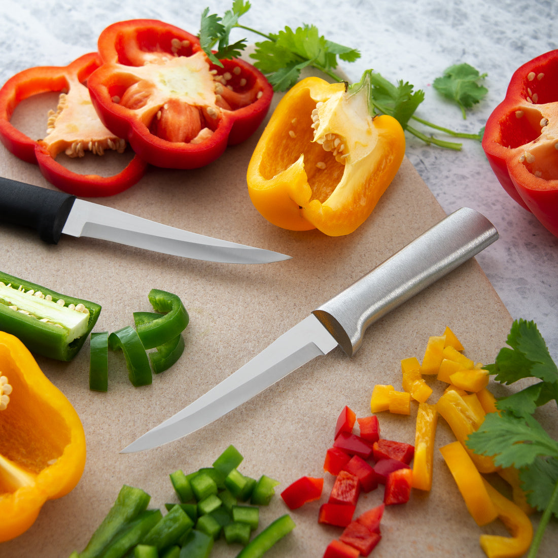 Silver handle and black handle Super Parer knives on a cutting board next to diced peppers