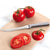 Silver handled tomato slicer on a tan cutting board next to sliced and whole tomatoes.