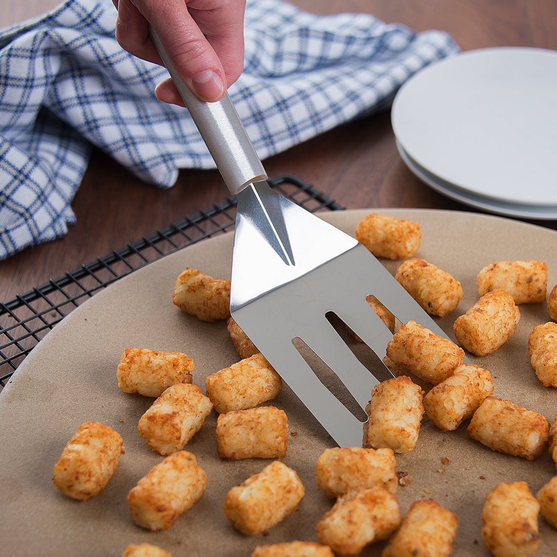 Silver handled Turnover scooping up tater tots on a pizza stone and cooling rack.