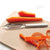 Aluminum handled vegetable peeler next to peeled carrots on a cutting board.